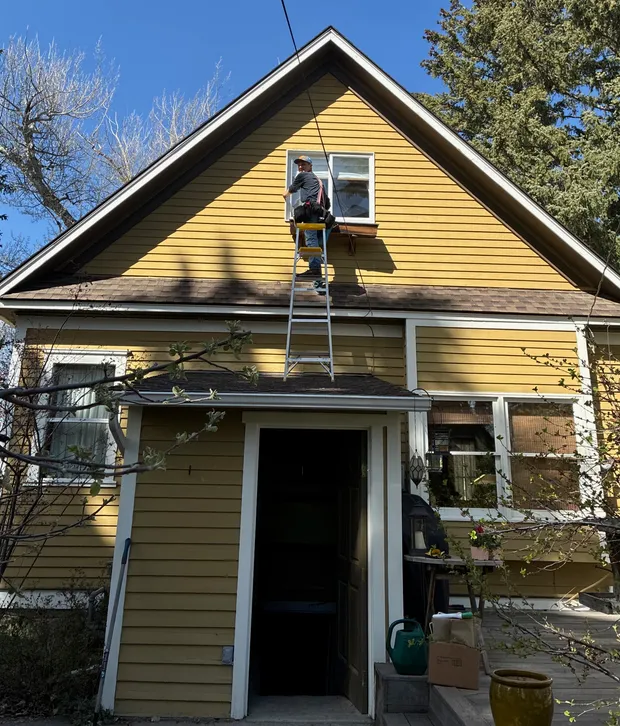 The owner high on a ladder cleaning the gable window of a historic yellow house